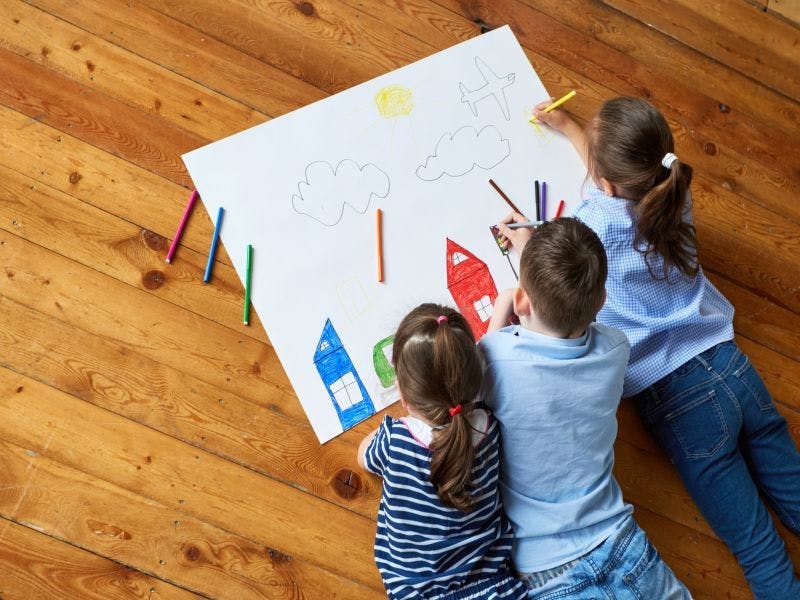 Three children happily engaged in colouring a picture together.