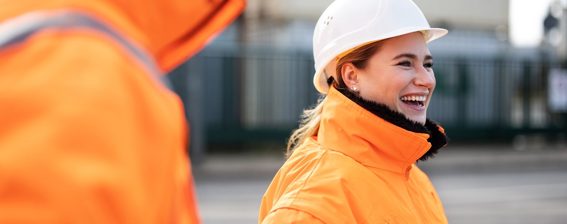 A woman wearing orange workwear and a safety helmet, smiling confidently.